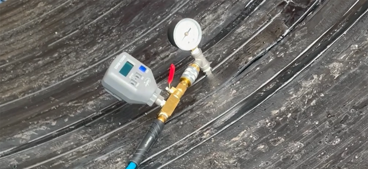 A pressure gauge and sensor connected to a blue hose on a black industrial surface.