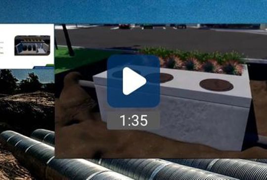 Screenshot of a paused video showing an underground concrete stormwater system with two circular grates.
