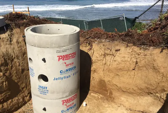 Concrete structure labeled "Reese Contech Jellyfish Filter" at a coastal excavation site near the ocean.