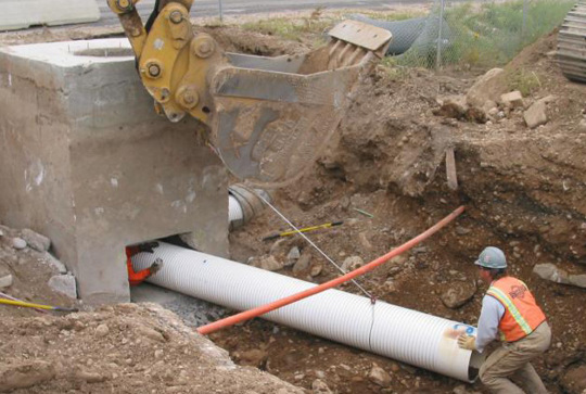 Construction worker installs a large pipe in a trench near heavy machinery at a building site.