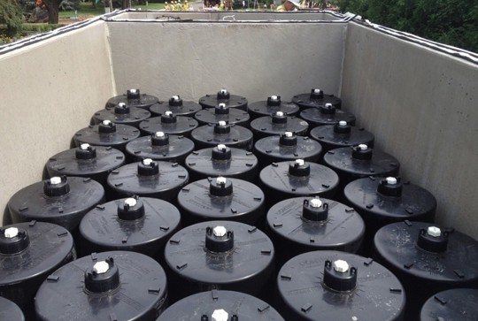 Multiple large StormFilter containers with white caps are arranged in rows inside a rectangular concrete enclosure.