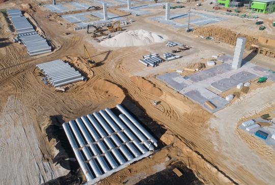 Aerial view of a construction site with piles of materials, machinery, and foundational structures in progress.