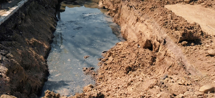 A muddy trench filled with water at a construction site, with piles of earth on both sides.