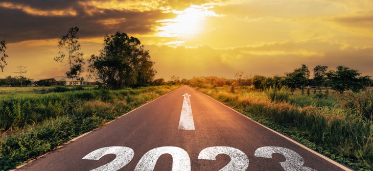 A road with "2023" painted on it leads towards a sunset, symbolizing a new journey or direction.