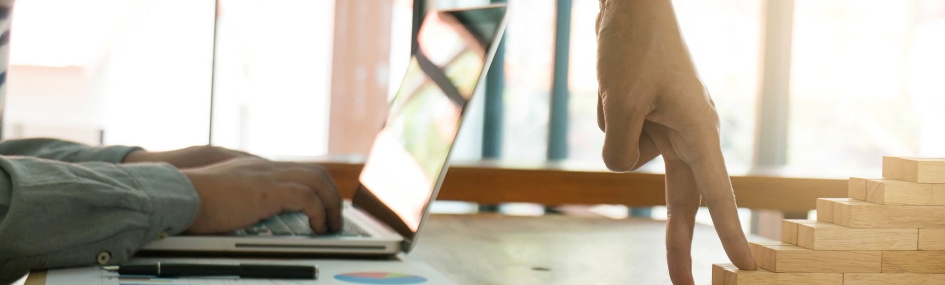Hand mimics walking up wooden blocks near a laptop on a desk with charts.
