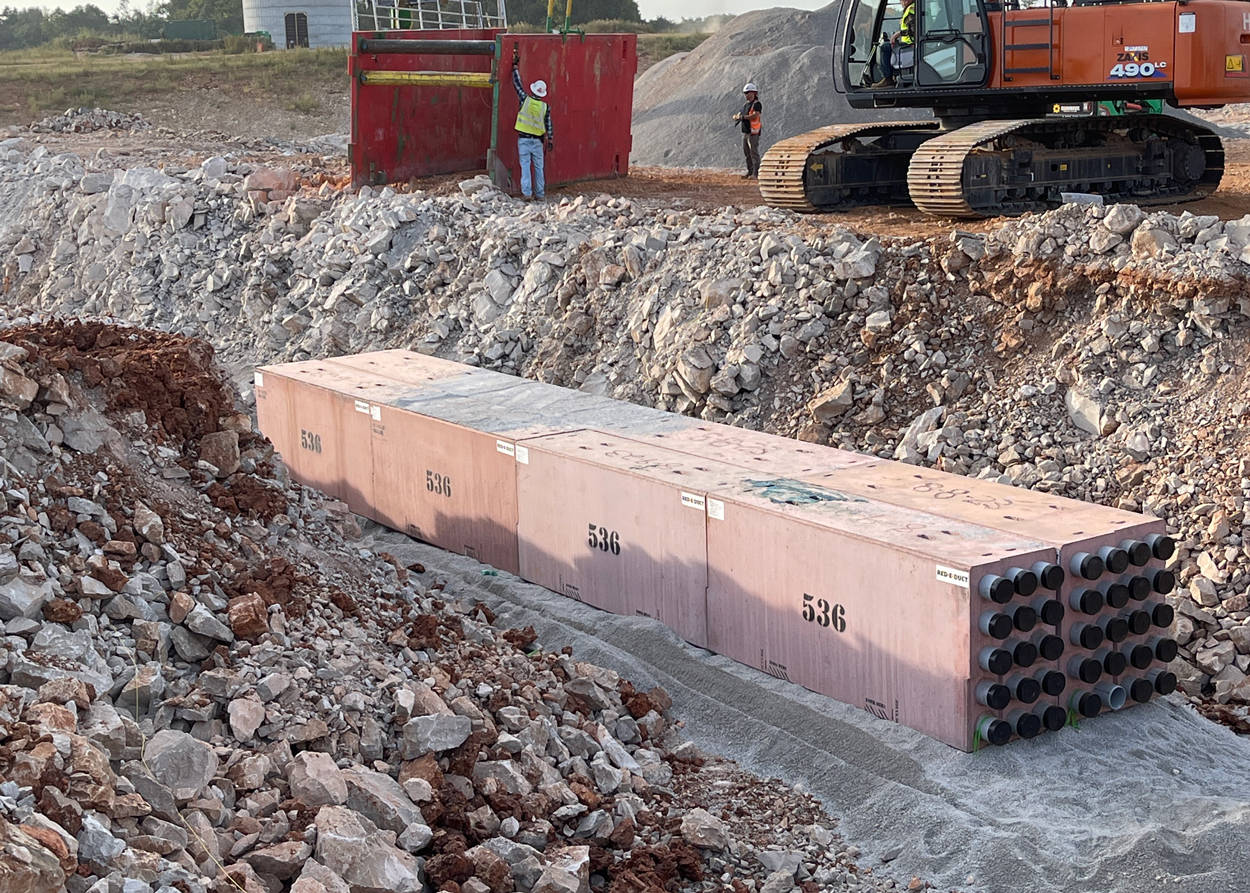 Large concrete utility duct banks marked "536" are laid in a trench at a construction site with workers and machinery nearby.