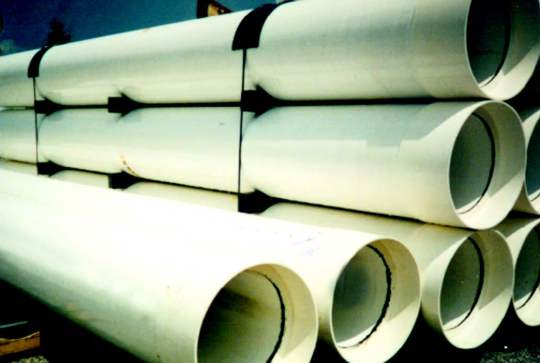 Stacks of large white industrial pipes secured with black straps, arranged horizontally on a wooden surface.