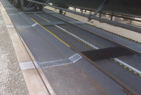 Railcar loading area with tracks, yellow safety lines, and metal grates, designed for efficient material transfer.