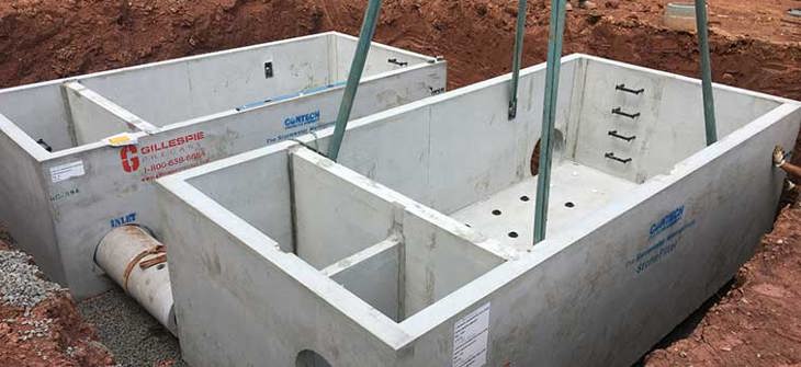 Installing large concrete septic tanks with workers guiding them into place using cranes at a construction site.